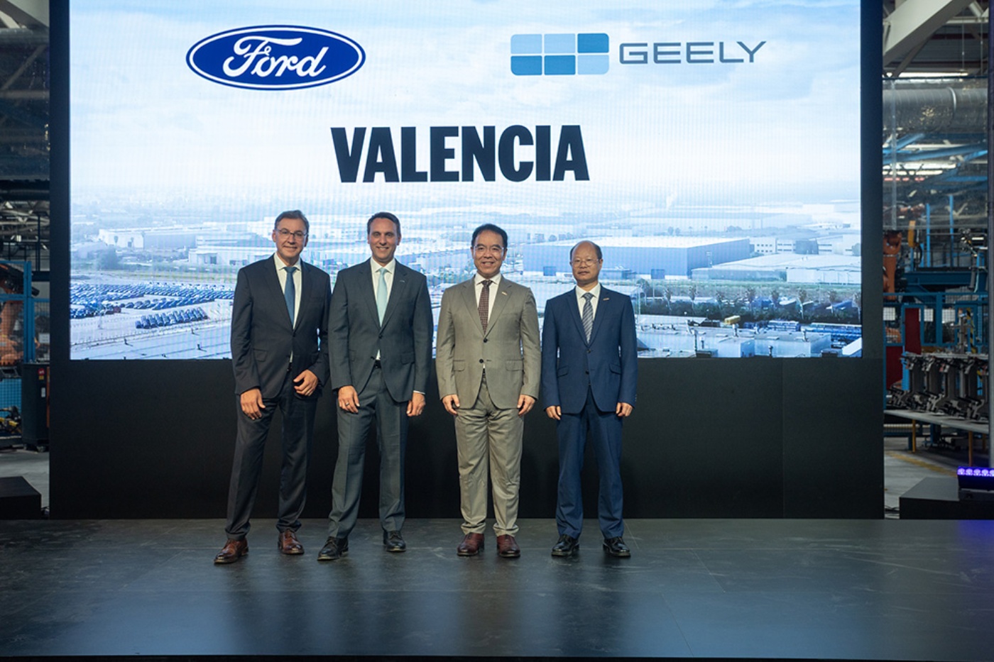 Four business leaders stand in front of a display showing the Ford and Geely logos and Valencia.