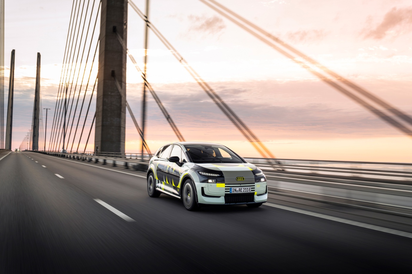Audi prototype electric vehicle driving across a bridge at sunset.