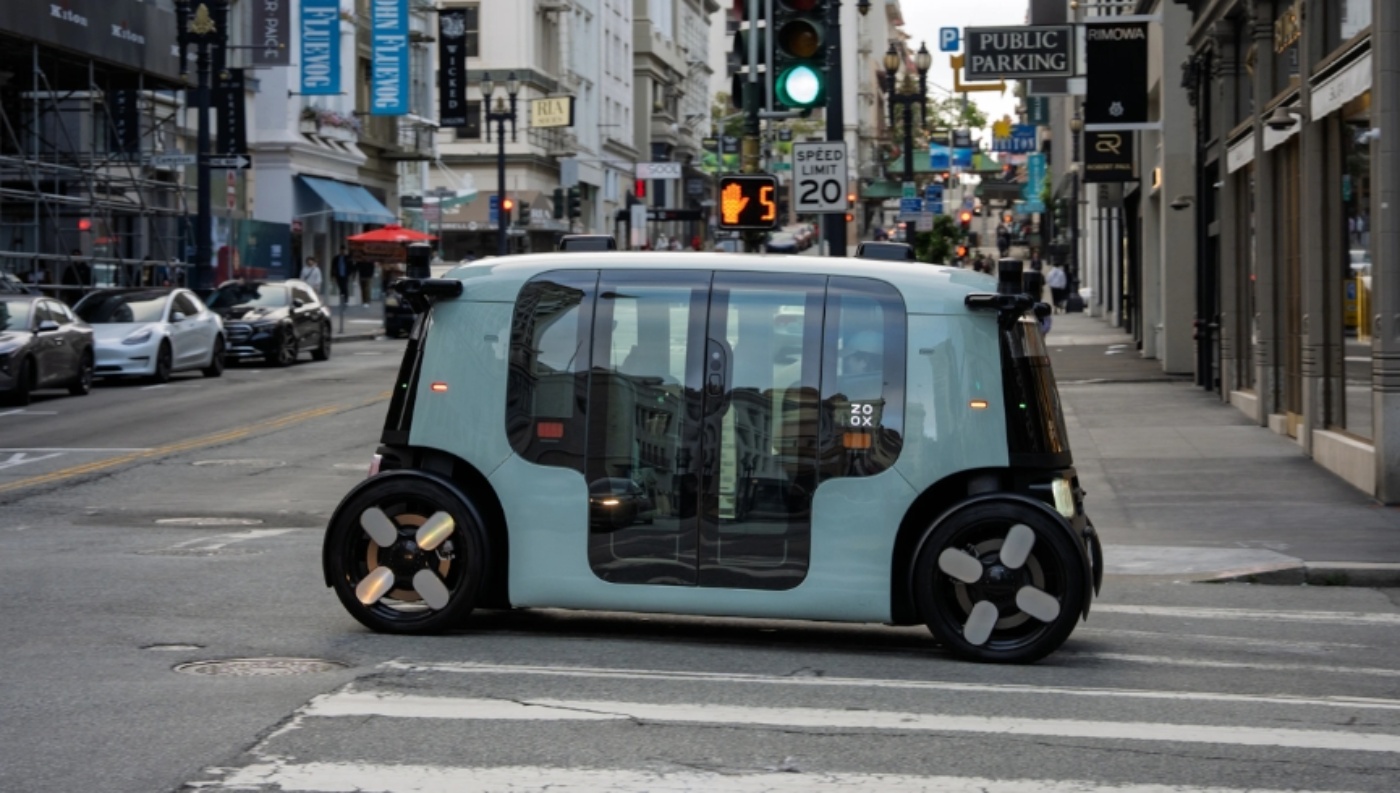 Zoox autonomous shuttle crossing a city street at an intersection.
