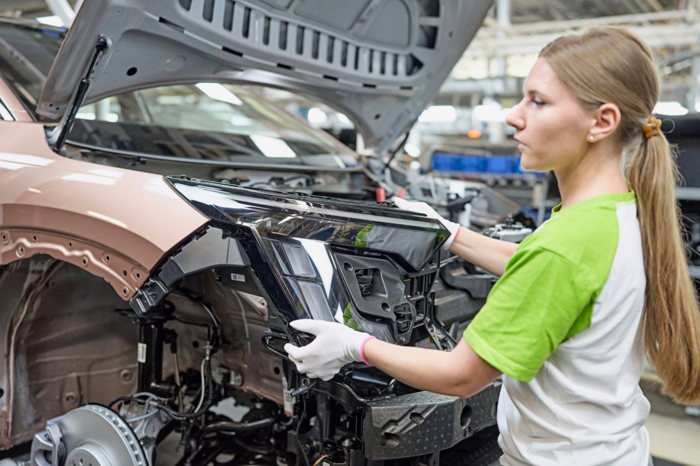 Mitarbeiterin arbeitet an der Front eines Fahrzeugs auf einer Produktionslinie.