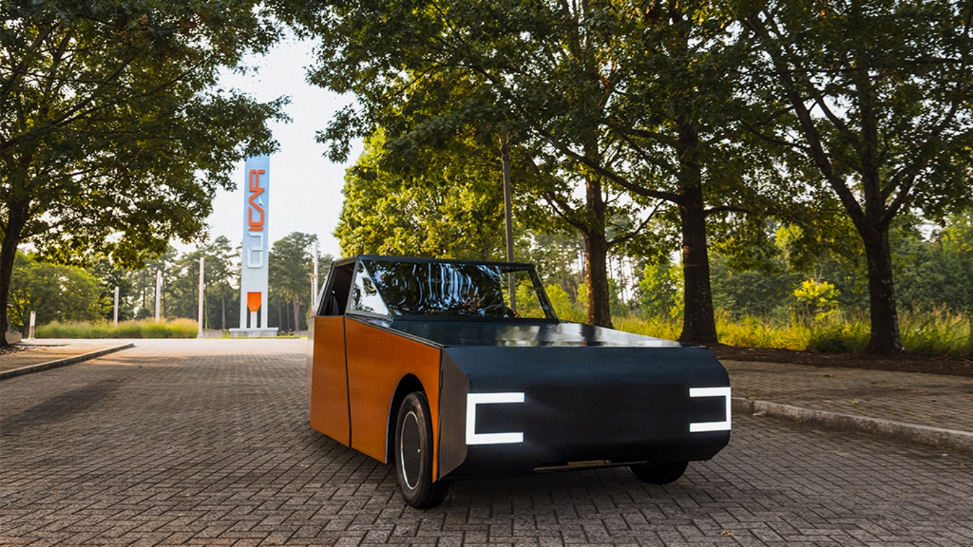 Orange autonomous vehicle from Clemson University driving on a tree-lined road.
