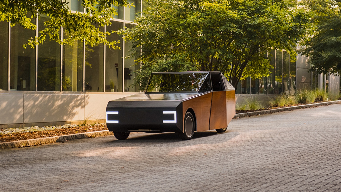 Orange autonomous vehicle from Clemson University driving on a tree-lined road.