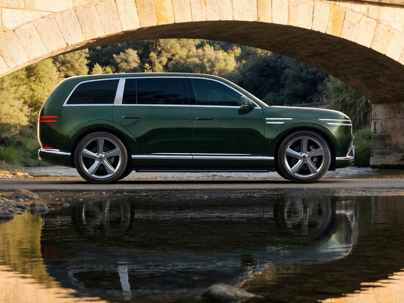 Grüner Genesis SUV unter einer Steinbrücke am Wasser.