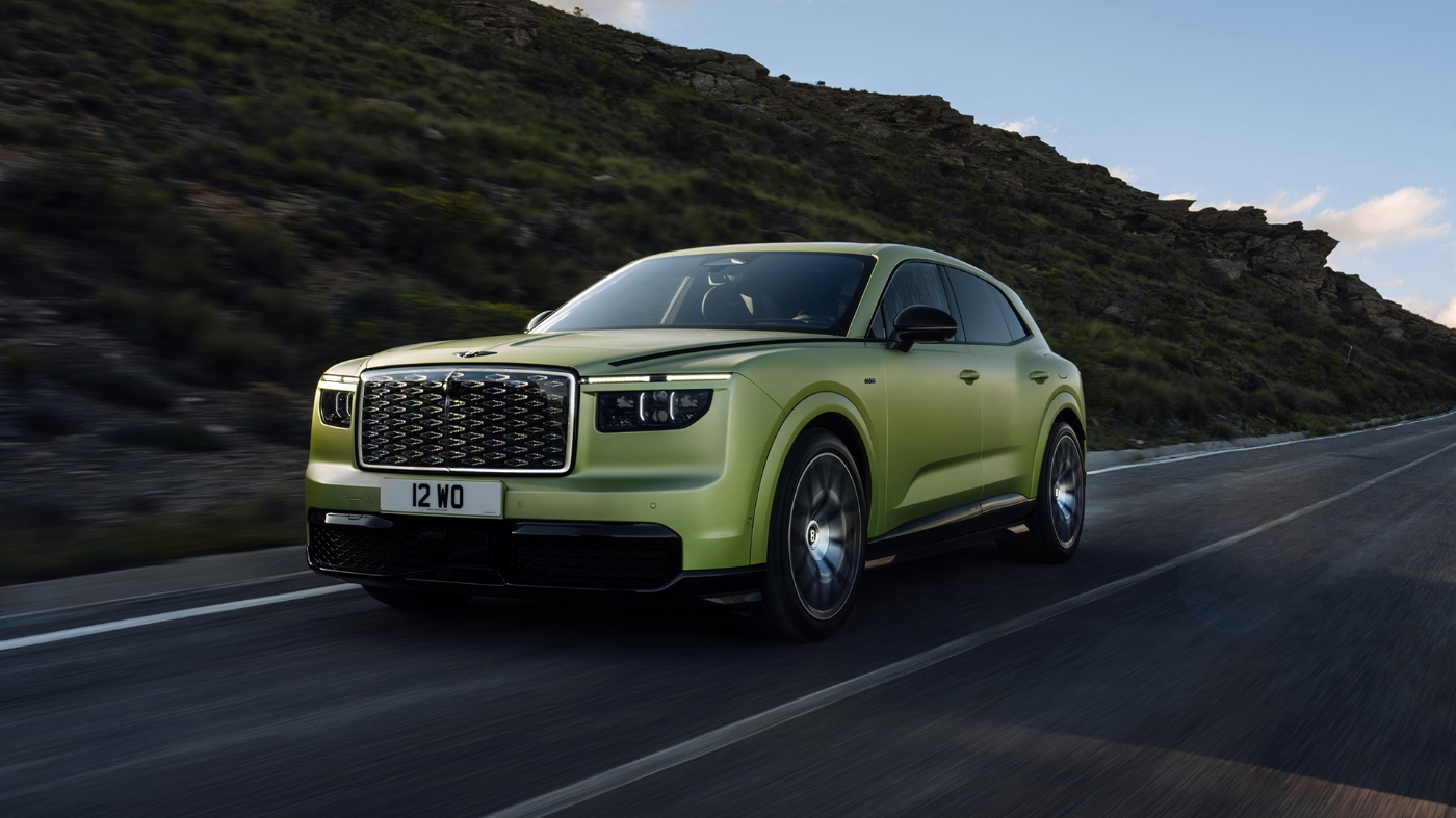 Green Bentley SUV driving on a winding mountain road.