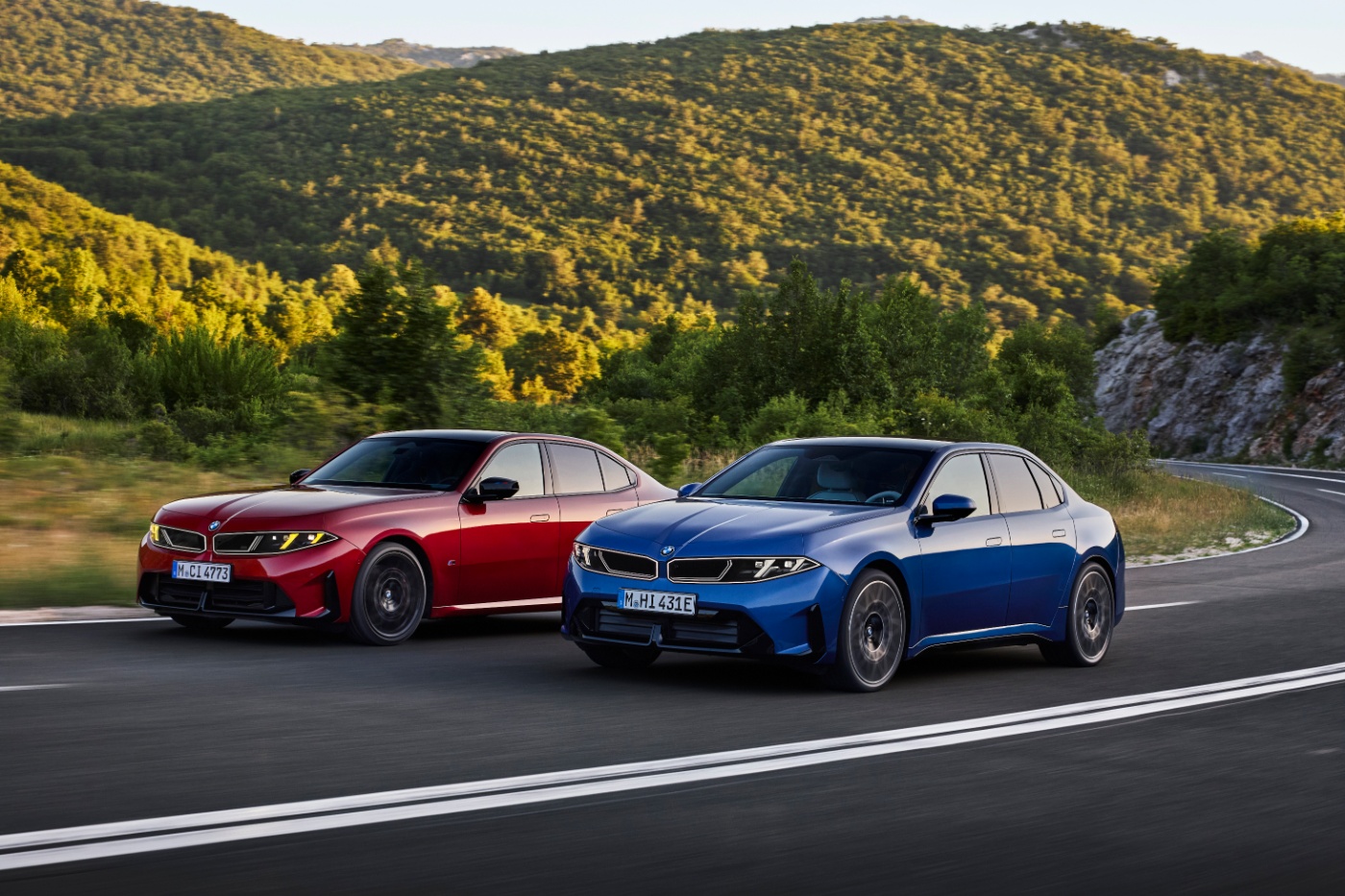 Red and blue BMW sedans driving side by side on a winding country road.