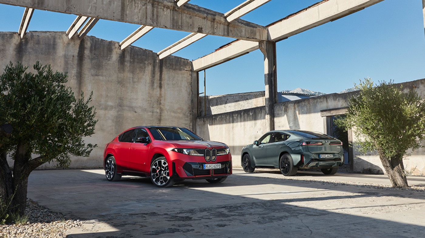 Ein roter und ein grauer BMW-SUV stehen in einem offenen Betongebäude mit sichtbaren Dachträgern.