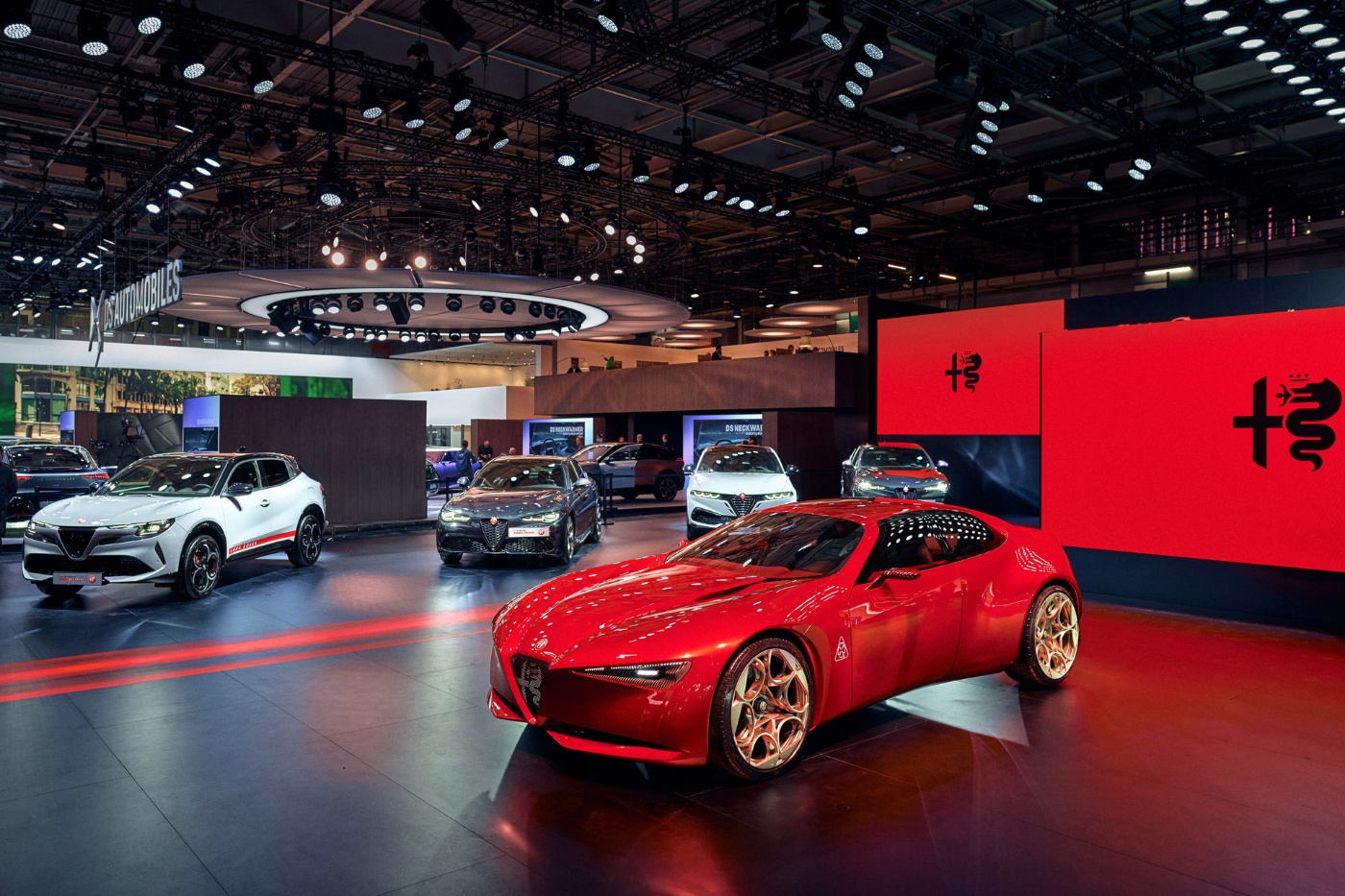 Roter Alfa Romeo Sportwagen auf einer Automesse mit weiteren Fahrzeugen im Hintergrund.