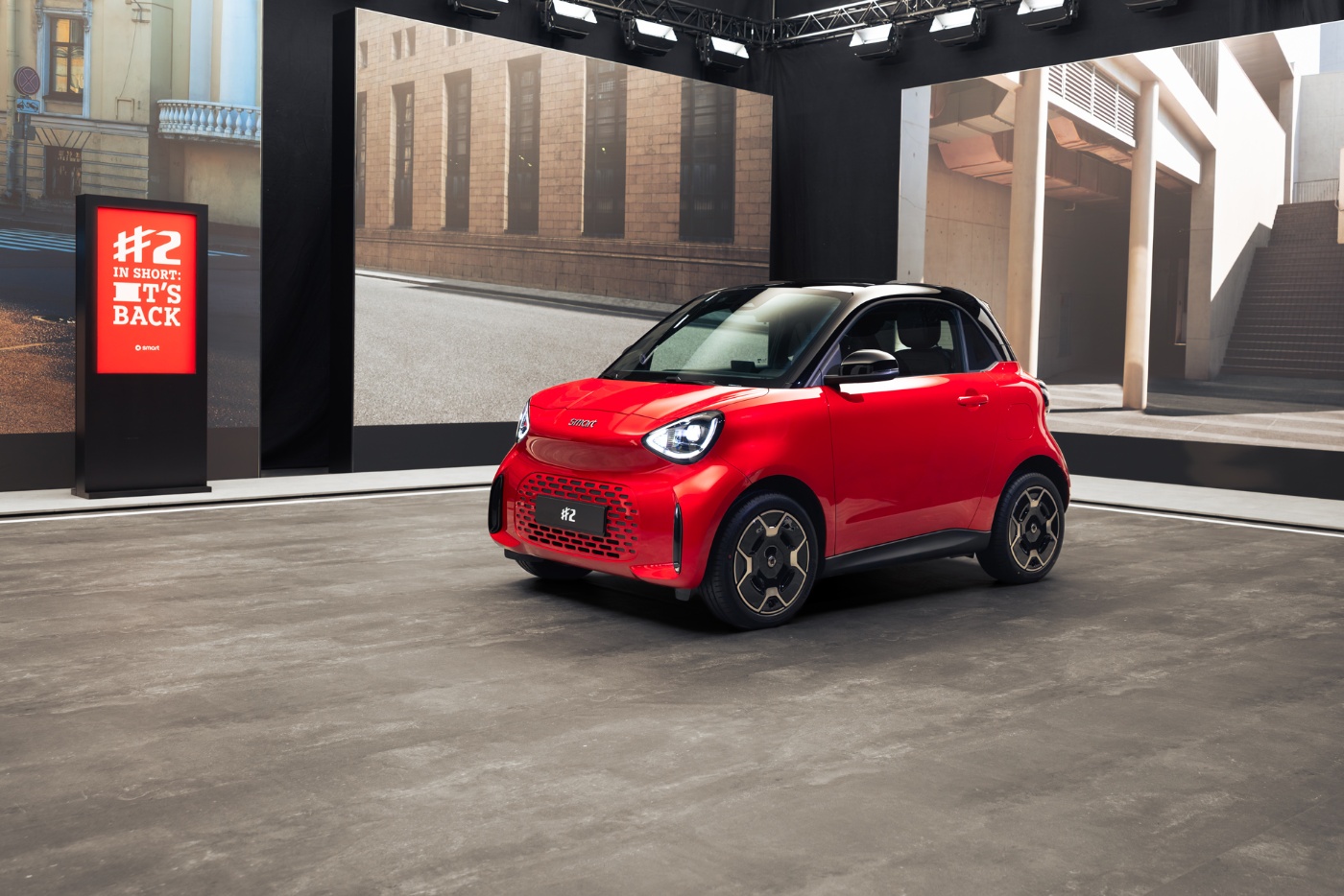 Rot-schwarzer smart Kleinwagen auf einer Automesse mit großer digitaler Anzeigetafel.
