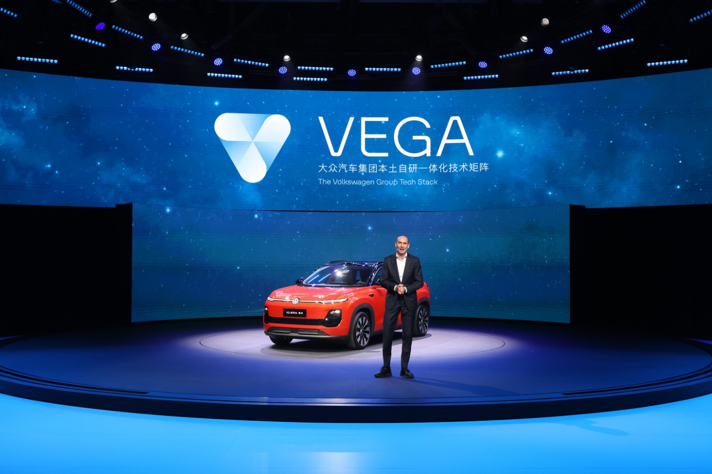 Präsentator neben einem roten ID. ERA 5X SUV auf der Bühne vor dem Volkswagen VEGA-Technologielogo.