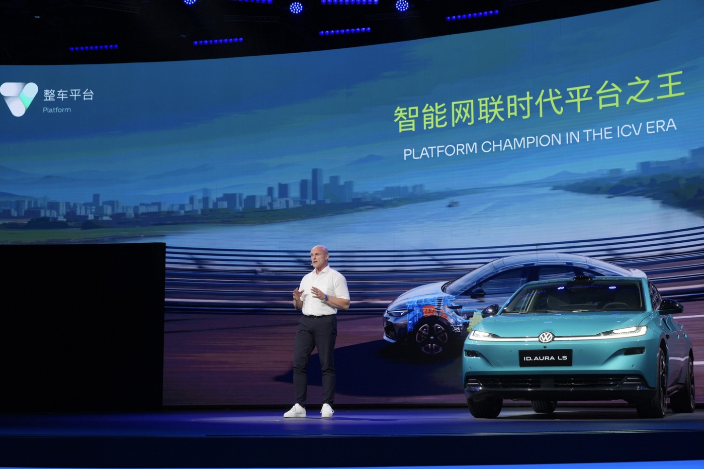 Präsentator neben einem Volkswagen-SUV auf einer Bühne mit chinesischem Text auf einer Leinwand.
