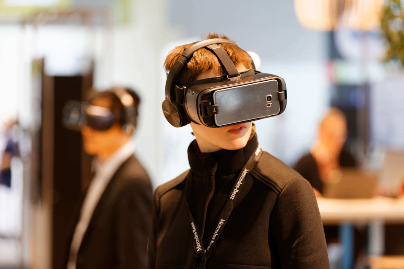 A person wears a VR headset at an exhibition with other visitors in the background.