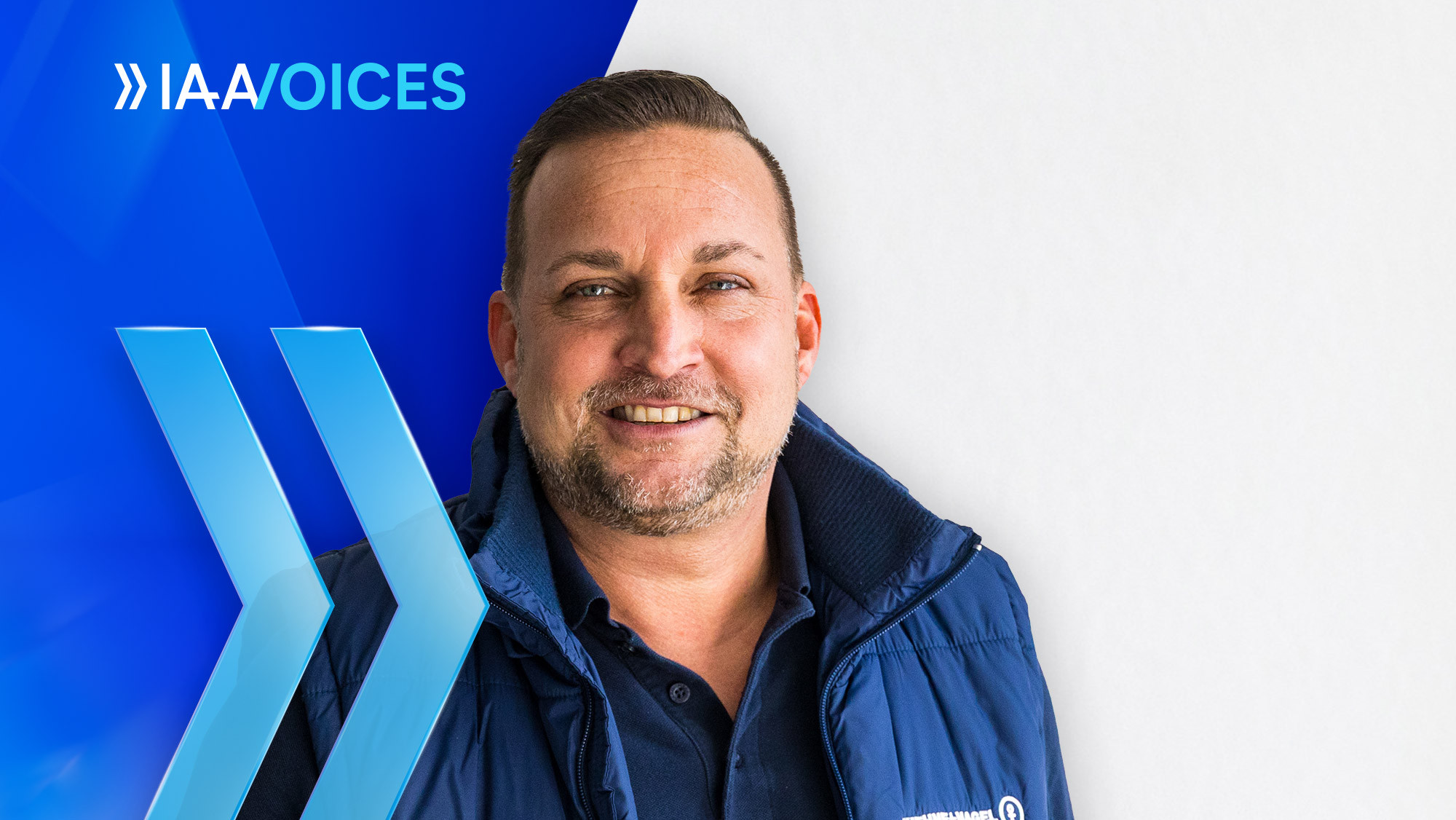 Smiling man in a blue jacket stands in front of a background with the text "IAA Voices".